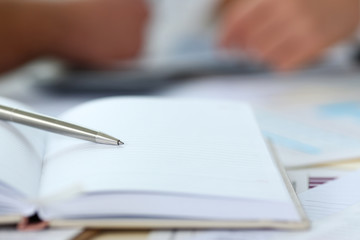 Silver pen lying on opened notebook sheet with people in background in office workplace closeup. Inspector occupation for student examination or career strategy personal training course signature