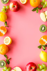 Oranges, lemon, apple, kiwi and grape - healthy food concept with fruits - on pink background top-down frame copy space