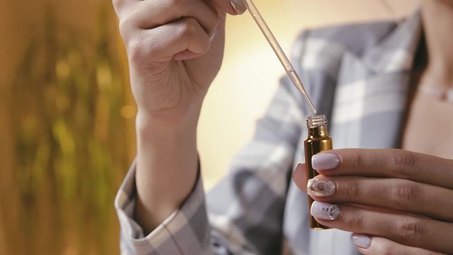 A beautiful young woman creates perfume in a glass bottle by combining several essential oils, close-up