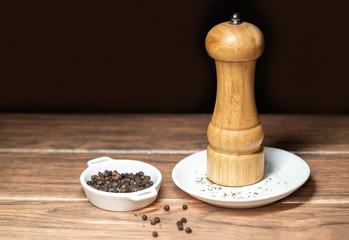 Molino de pimienta negra con granos de pimienta sobre un plato de ceramica blanca 