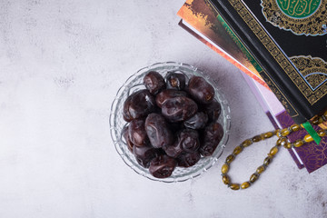ramadan celebration concept. dates inside glass bowl beside religion book and quran with rosary beads or tasbih. selective focus on foreground.