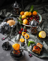 tea armud in Turkish style with lemon. served on a silk tablecloth with baklava and fruit-cherries and apricots