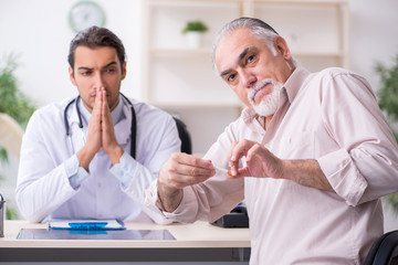 Obraz premium Young male doctor and old patient in antismoking concept