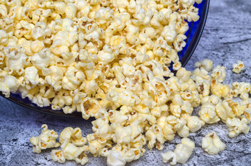 popcorn spilled out of a glass bowl on a gray abstract background