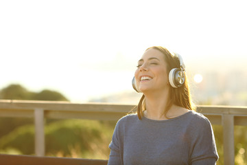 Happy girl listening music on headphones at sunset