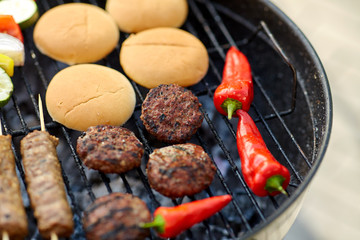 cooking, barbecue and food concept - close up of shish kebab meat, vegetables on bamboo skewers, burger buns and cutlets roasting on brazier grill