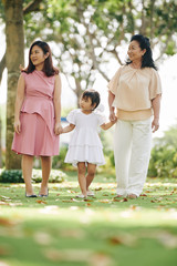 Fototapeta premium Pretty young smiling grandmother, mother and daughter holding hands when walking in summer park