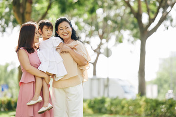 Mother and grandmother carrying adorable little girl when walking in park together