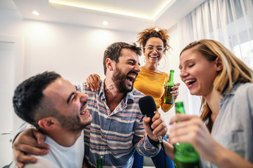 Group of best friends having fun at home. They are drinking beer and having karaoke night.