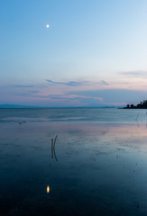 Moon above a lake with its reflection on the Trasimeno lake surface at dusk