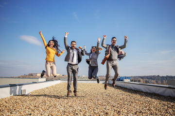 Four excited happy business people jumping on rooftop and cheering for success.