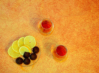 Two glass glasses with cognac and a plate with chocolate candies and cut lemon on a brown abstract...