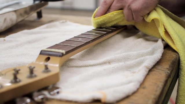 Man cleaning the fretboard of a guitar that he is refinishing.