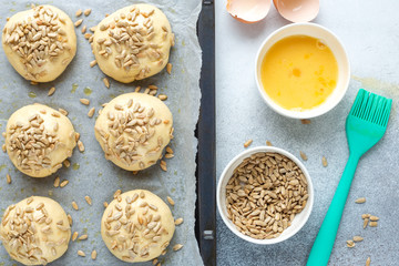 Pieces of raw dough on a pan, silicone brush, egg, seeds. Cooking homemade buns. Top view