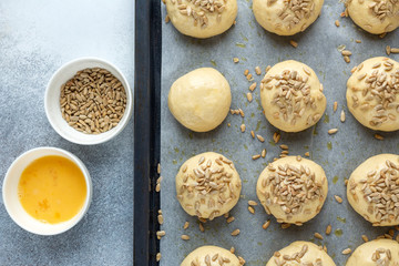 Raw dough balls sprinkled with seeds on pan. Cooking homemade buns. Top view