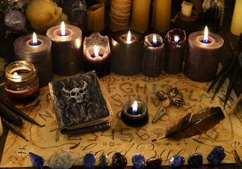 Old book with devil face on cover, black candles and ouija spiritual board.