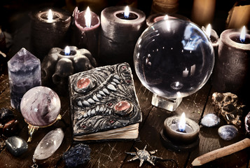 Evil book, crystal ball and black candles on witch table.