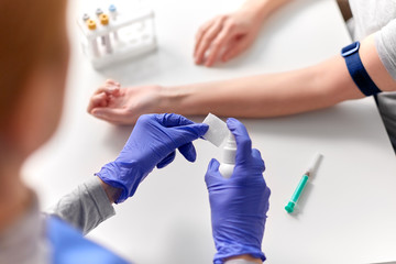 medicine, healthcare and diabetes concept - close up of doctor in gloves with sanitizer disinfecting wipe before taking blood from patient's hand for test at hospital