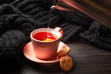 Cup of tea with lemon and cookies, water pouring from electric kettle into pink cup