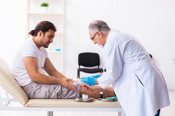 Fototapeta premium Leg injured man visiting old doctor in first aid concept