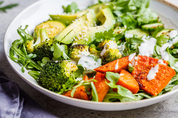 Vegan salad bowl with baked vegetables, avocado and tahini dressing in a gray bowl.