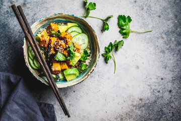 Vegan tofu poke bowl with rice, cucumber, avocado and nori, gray background, top view.