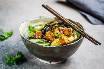 Vegan tofu poke bowl with rice, cucumber, avocado and nori, gray background.
