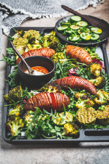 Baked vegetables salad with tahini dressing on a cast-iron pan. Baked sweet potato, broccoli and zucchini with arugula. Healthy vegan food concept.