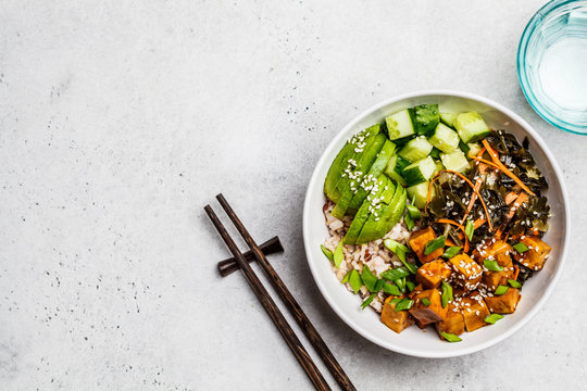 Vegan ahi poke bowl with tofu, rice, seaweed, avocado and cucumber, white background, top view.