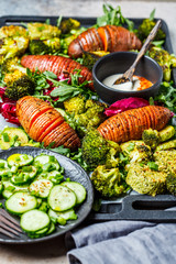 Baked vegetables salad with tahini dressing on a cast-iron pan. Baked sweet potato, broccoli and zucchini with arugula. Healthy vegan food concept.