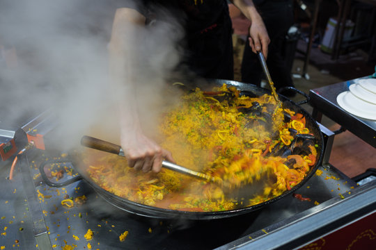 Person mixing paela in large cast iron frying pan