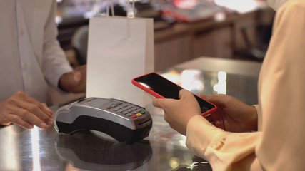 An upwardly mobile Asian Muslim woman using a mobile phone - smartwatch to pay for a product at a sale terminal with nfc identification payment for verification and authentication