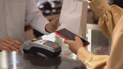 An upwardly mobile Asian Muslim woman using a mobile phone - smartwatch to pay for a product at a sale terminal with nfc identification payment for verification and authentication