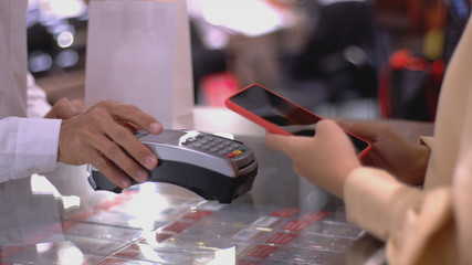 An upwardly mobile Asian Muslim woman using a mobile phone - smartwatch to pay for a product at a sale terminal with nfc identification payment for verification and authentication