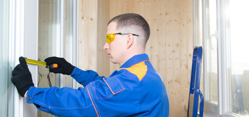 a worker in a blue uniform measures the wooden window opening with a meter