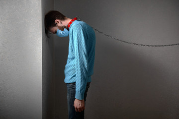 man in medical mask, in a collar on a chain staying depressed in corner