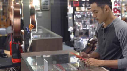 An upwardly mobile Asian Muslim man using a mobile phone - smartwatch to pay for a product at a sale terminal with nfc identification payment for verification and authentication