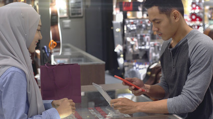 An upwardly mobile Asian Muslim man using a mobile phone - smartwatch to pay for a product at a sale terminal with nfc identification payment for verification and authentication