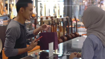 An upwardly mobile Asian Muslim man using a mobile phone - smartwatch to pay for a product at a sale terminal with nfc identification payment for verification and authentication
