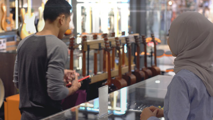 An upwardly mobile Asian Muslim man using a mobile phone - smartwatch to pay for a product at a sale terminal with nfc identification payment for verification and authentication