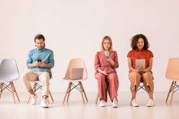 Obraz premium Serious young multi-ethnic people immersed in social media sitting on chairs in row and using modern gadgets