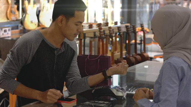 An upwardly mobile Asian Muslim man using a mobile phone - smartwatch to pay for a product at a sale terminal with nfc identification payment for verification and authentication
