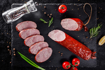 Various sausages and smoked products lie on a black board, sausage, sausages, ribs, rolls. Top view, overhead. Flat lay