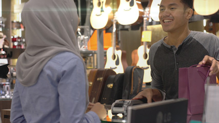 An upwardly mobile Asian Muslim man using a mobile phone - smartwatch to pay for a product at a sale terminal with nfc identification payment for verification and authentication