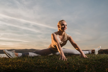 A beautiful woman, a fitness instructor, in light clothing, trains on the beach, against the sky. Shows exercises from yoga, Pilates, Deep Work, Step aerobics