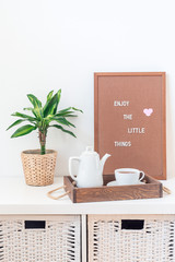 Home interior with white chest of drawers, green palm in  pot, wooden tray with tea, and pegboard with the inspiring phrase, Scandinavian style, minimalistic concept, vertical