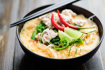 Spicy rice noodles soup with spices and herbs (Thai Tom Yum) in a bowl with chopsticks, Asian food