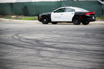 Tire marks in the road from cars doing donuts and a blurred police car in the background. 