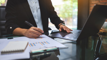 A businesswoman writing and working on business financial data and document with laptop computer on the table in office
