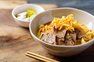 Northern Thai food (Khao Soi), spicy curry noodles soup with coconut milk and beef in a bowl on wooden background